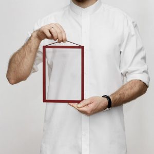 Ein Mann in einem weissen Hemd hält einen kleinen roten Bilderrahmen in der Hand.
